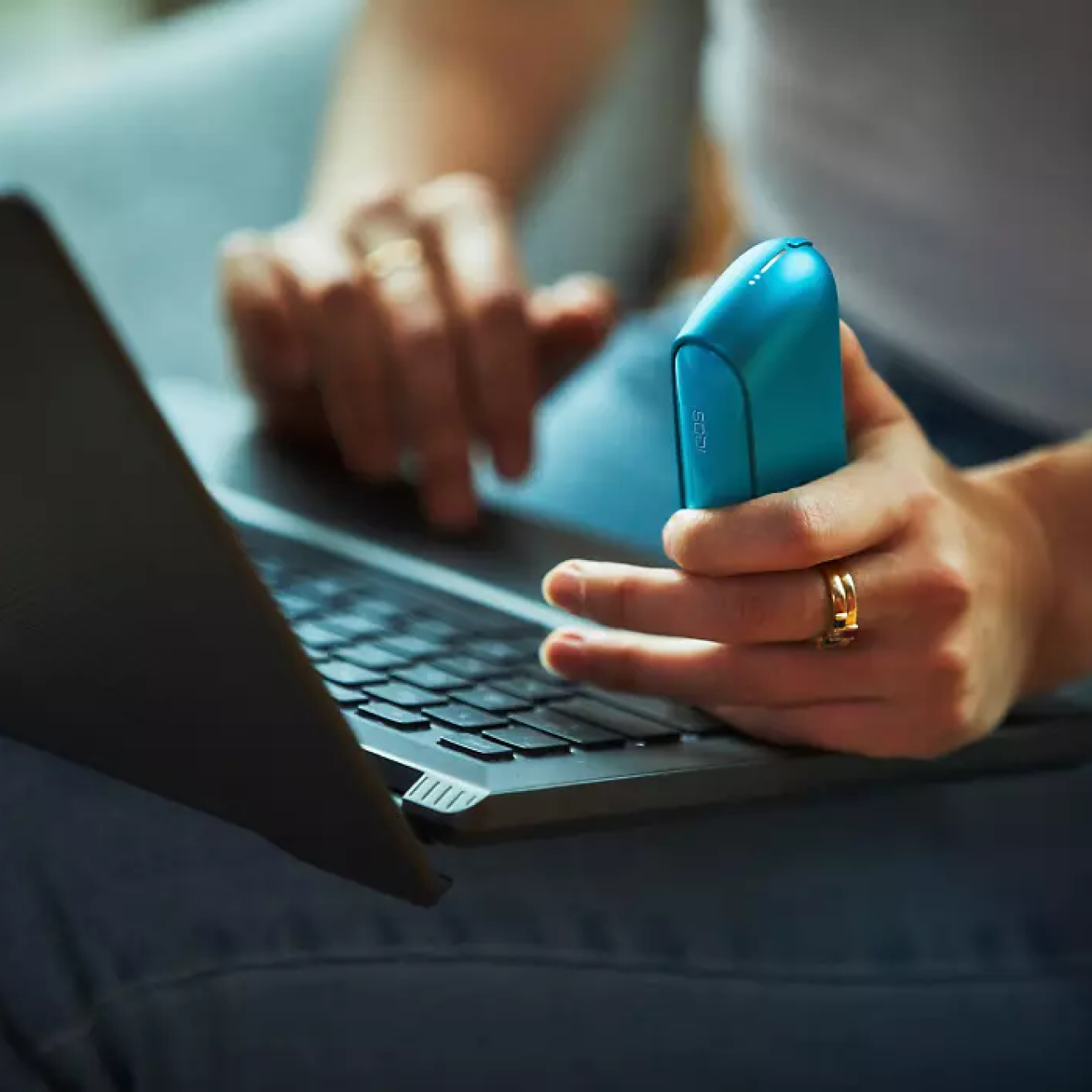 Muž sediaci pri pracovnom stole u PC držiaci IQOS.