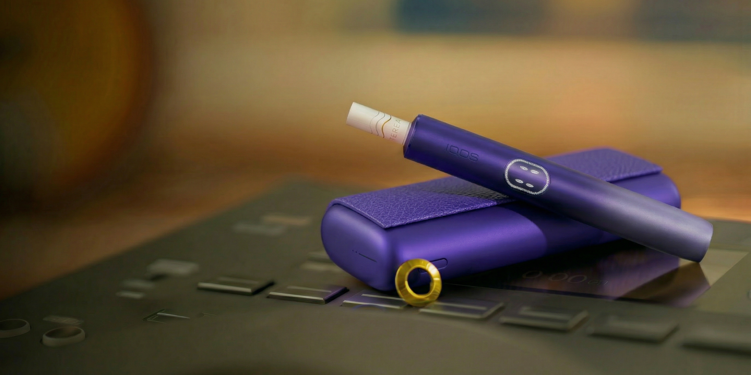 Zariadenie IQOS ILUMA i PRIME vo fialovejj farbe nad svojou nabíjačkou, upravené obalom a ozdobnými krúžkami.