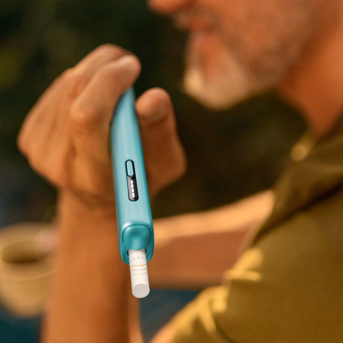 Person holding IQOS ILUMA i ONE with tobacco stick inserted