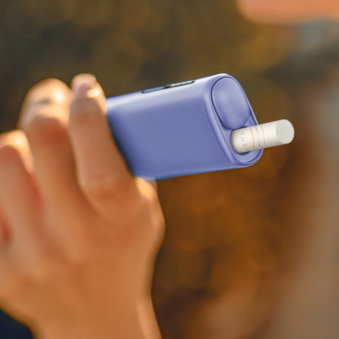 Person holding IQOS ILUMA i ONE with tobacco stick inserted