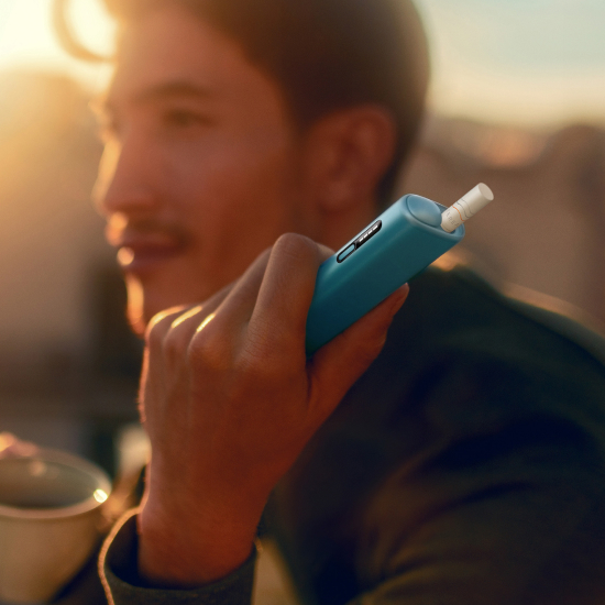 Person holding IQOS ILUMA i ONE with tobacco stick inserted