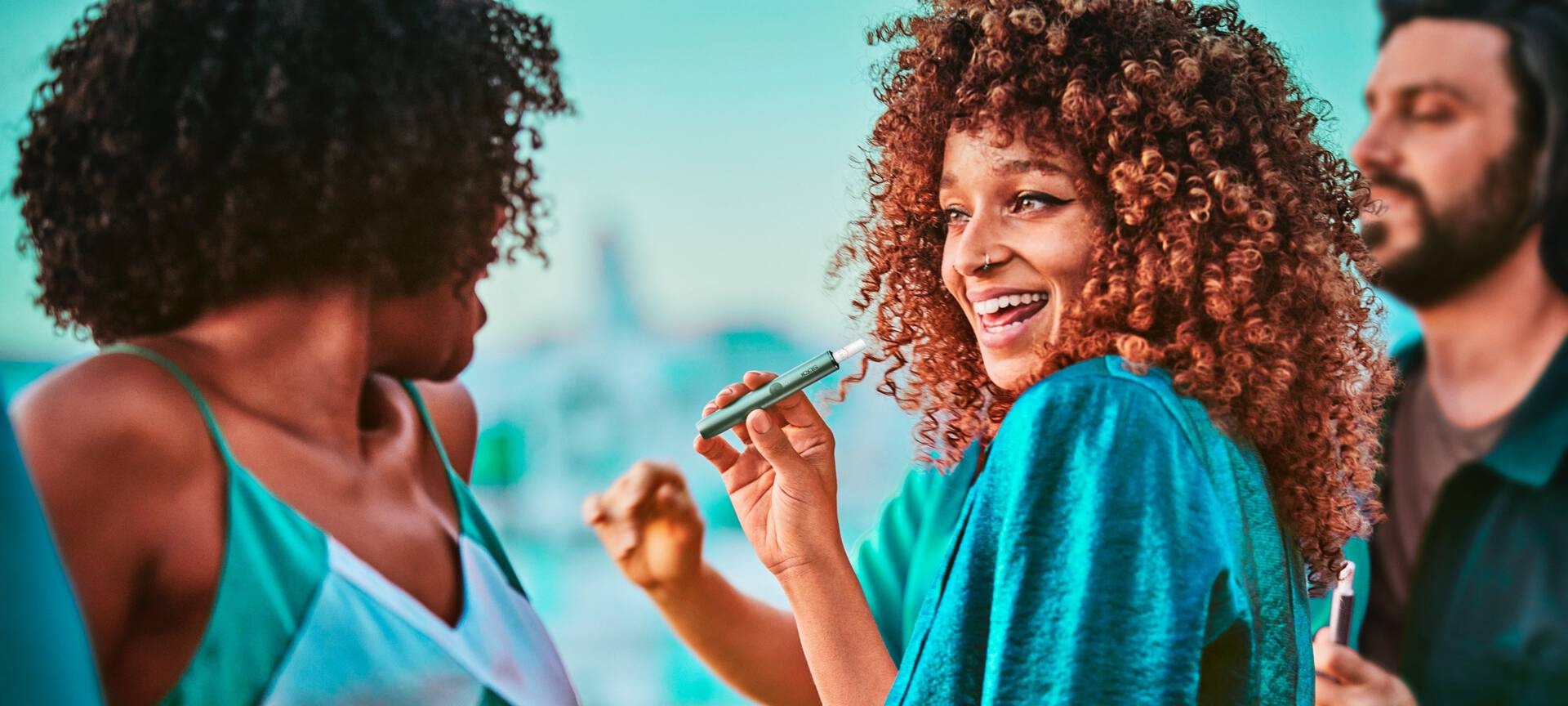 A group of friends, one woman holding a Jade Green IQOS ILUMA Holder.