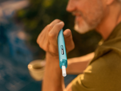 Hand holding a IQOS Iluma I One device on a dark background