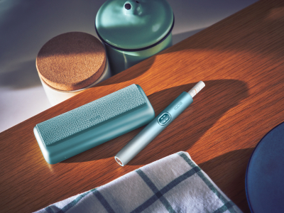 Blue IQOS ILUMA i PRIME device and its charger on a wooden table