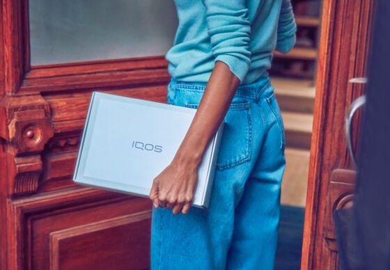 A person in jeans carrying a package from IQOS.