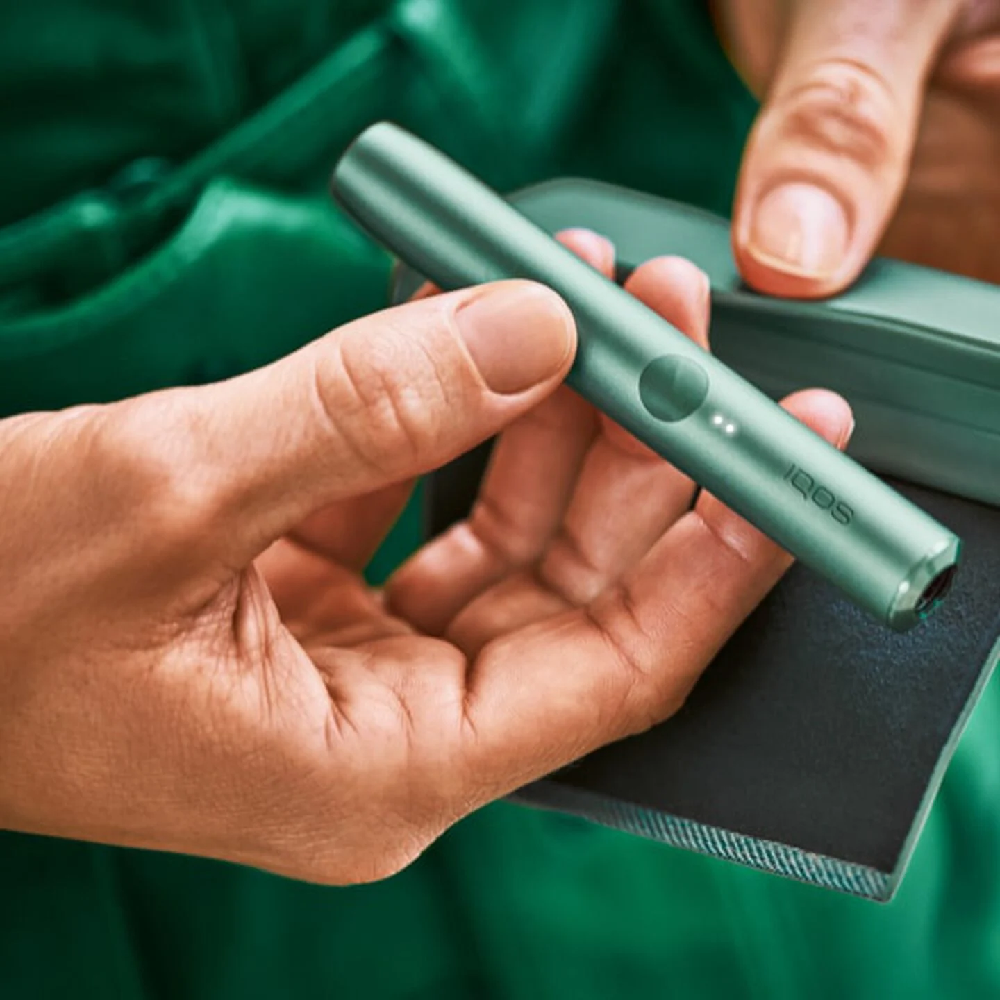 A person placing an IQOS ILUMA Pocket Charger into a charging station.
