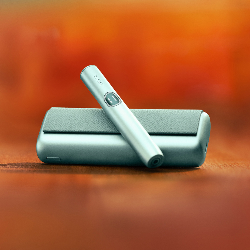 Breeze Blue IQOS ILUMA i PRIME device and its charger on a brown table
