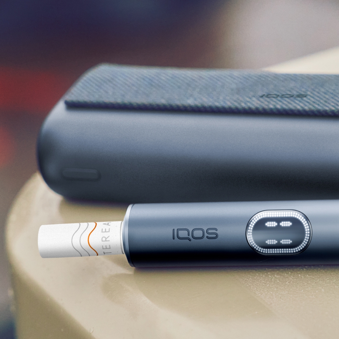 Black IQOS ILUMA i PRIME device and its charger on a brown table