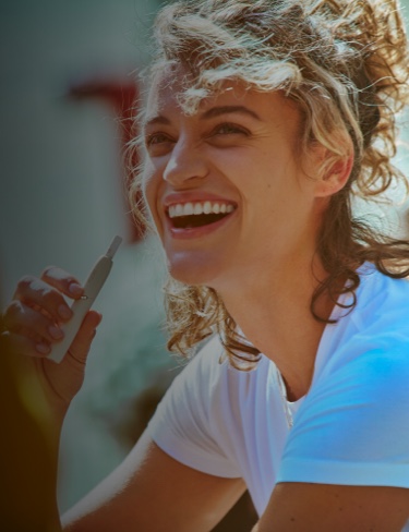 Smiling woman holding a white IQOS 3 holder with HEETS stick