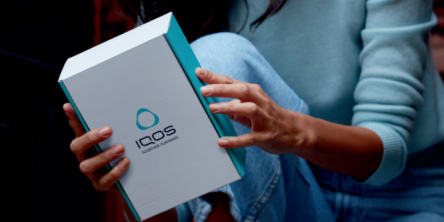 One person handing an IQOS device box to a smiling woman. One person handing an IQOS device box to a smiling woman.
