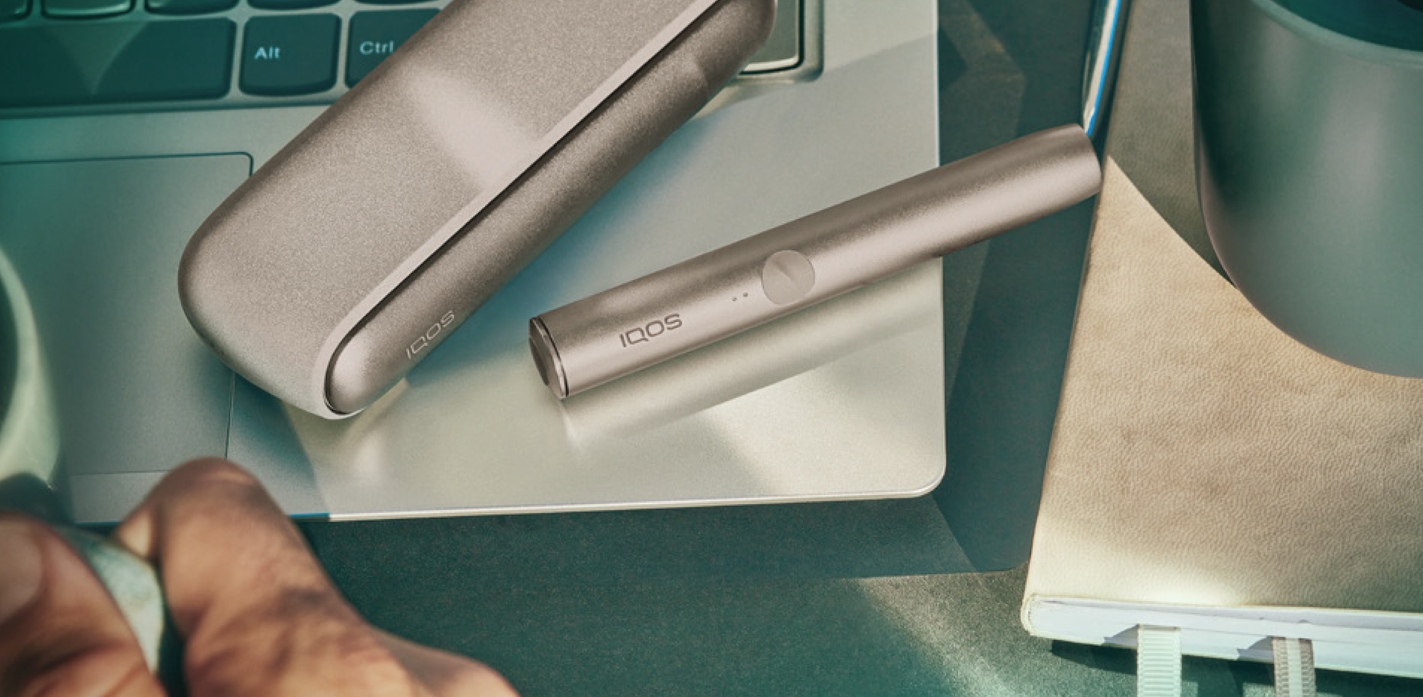 A woman holding an IQOS device looking at a laptop.