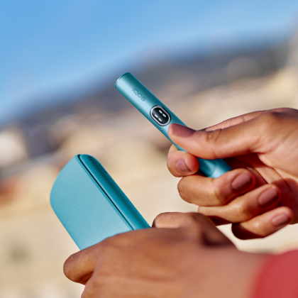 Close-up of a user holding the IQOS ILUMA i holder and pocket charger desktop version