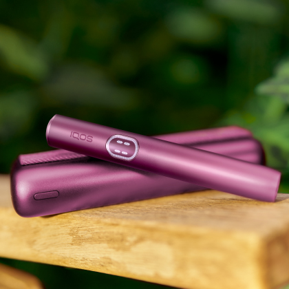 IQOS ILUMA i Prime pocket charger and holder placed together on a wooden surface, highlighting their new touchscreen feature.