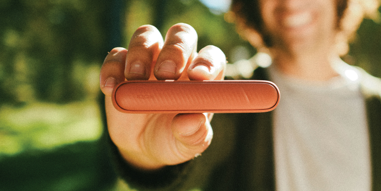Person holding an IQOS ILUMA i device outdoors