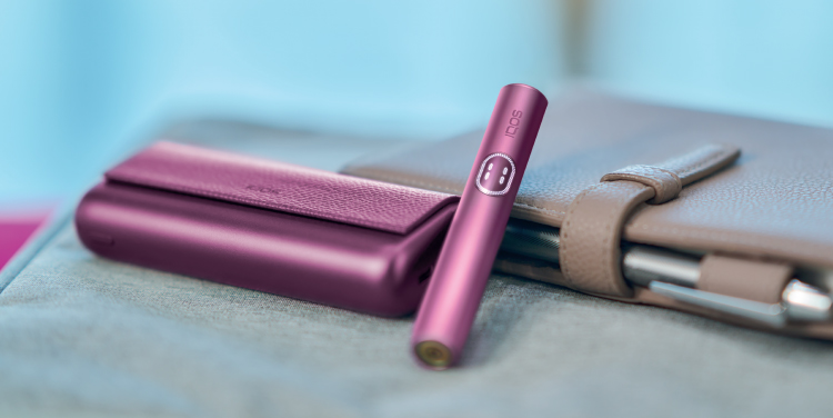 IQOS ILUMA i Prime device placed on the desk beside a book