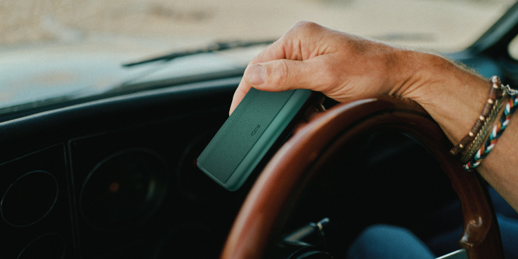 A hand holding IQOS ILUMA i Prime device inside a car