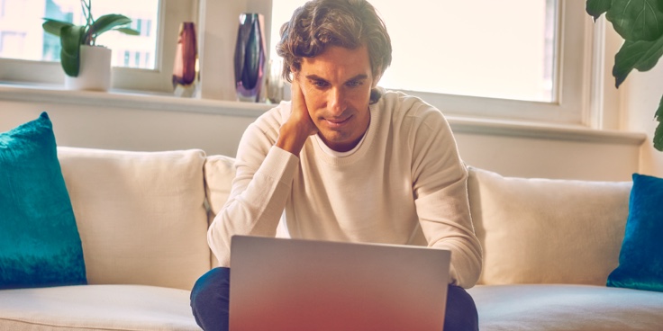 A man sitting on a couch looking at a laptop.