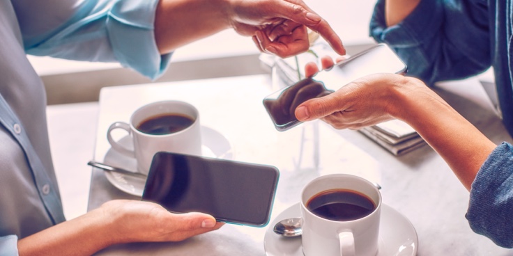 Two people holding phones over two cups of coffee. Two people holding phones over two cups of coffee.