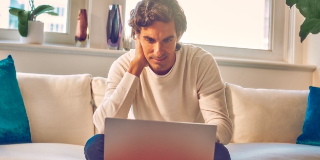 A man sitting on a couch looking at a laptop.