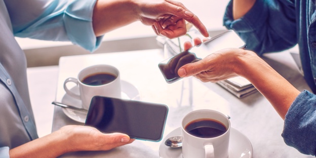 Two people holding phones over two cups of coffee. Two people holding phones over two cups of coffee.