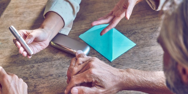 A hand showing an IQOS device to another person. A hand showing an IQOS device to another person.