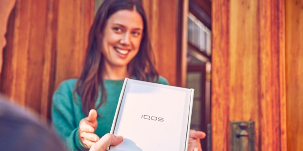 One person handing an IQOS device box to a smiling woman. One person handing an IQOS device box to a smiling woman.