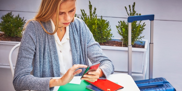 A woman sitting at a table next to her suitcase with a smartphone, passport and plane ticket. A woman sitting at a table next to her suitcase with a smartphone, passport and plane ticket.