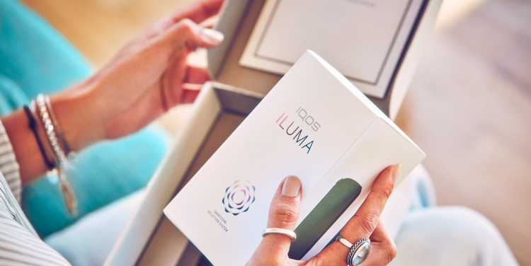 A person holding an IQOS ILUMA box. A person holding an IQOS ILUMA box.