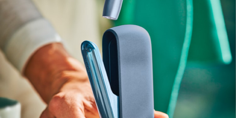 A person placing an IQOS ILUMA Pocket Charger into a charging station.