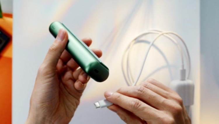 Hands plugging an IQOS ILUMA ONE into a power adaptor.