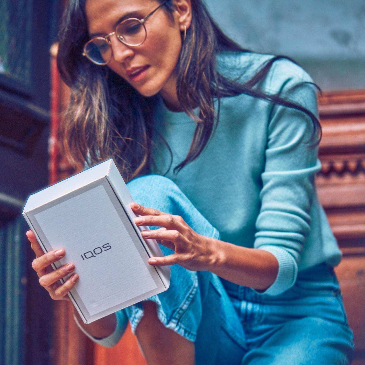 A woman looking at the back of an IQOS box.