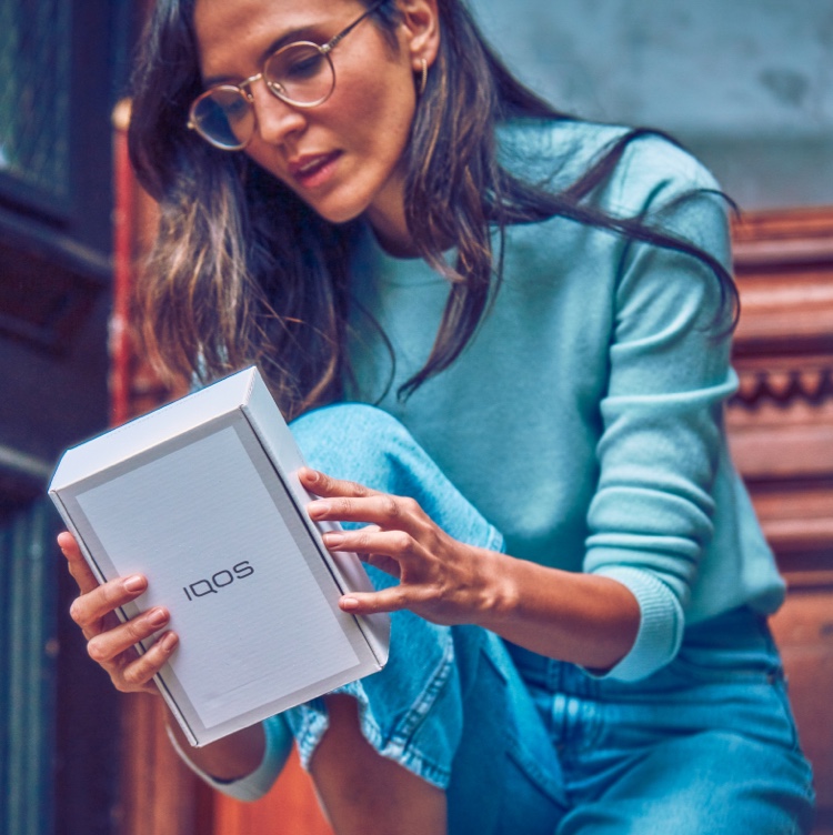 A woman looking at the back of an IQOS box.