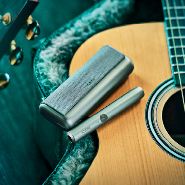 A Jade Green IQOS ILUMA PRIME Holder and Pocket Charger on a guitar..