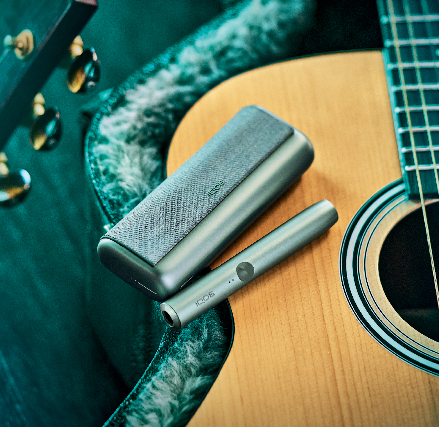 A Jade Green IQOS ILUMA PRIME Holder and Pocket Charger on a guitar..