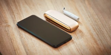 A mobile and a gold IQOS kit on a table A mobile and a gold IQOS kit on a table