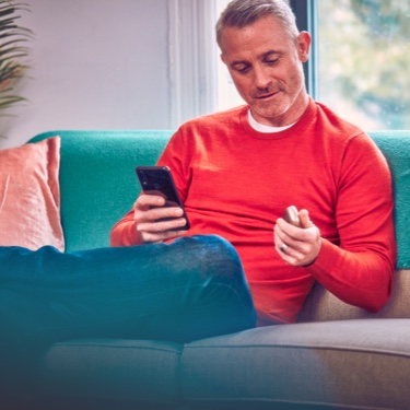Hombre con el celular en una mano y un dispositivo IQOS en la otra, siguiendo instrucciones Hombre con el celular en una mano y un dispositivo IQOS en la otra, siguiendo instrucciones
