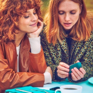 Dos mujeres mirando un dispositivo IQOS azul claro Dos mujeres mirando un dispositivo IQOS azul claro