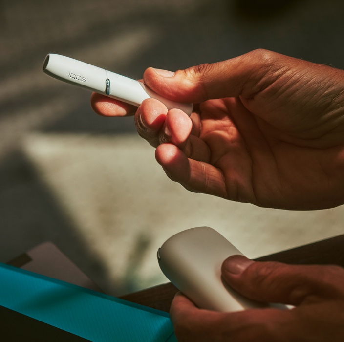 IQOS in white, holder in right hand, charger in left 