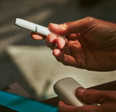IQOS in white, holder in right hand, charger in left 