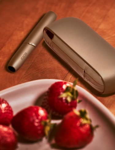 A gold IQOS device next to a bowl of fruit. 