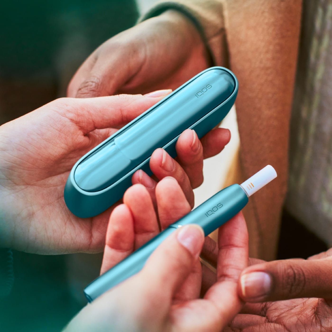 Person überreicht das IQOS ORIGINALS DUO in Turquiose an andere Person.