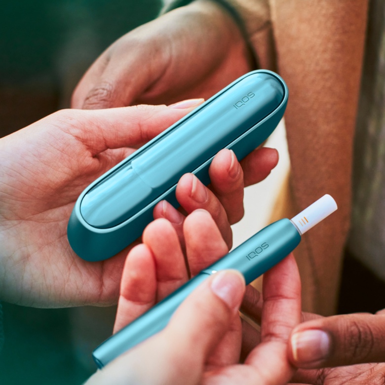 Person überreicht das IQOS ORIGINALS DUO in Turquiose an andere Person.
