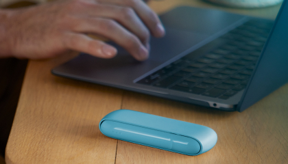 Hands typing on laptop and Iphone next to turquoise IQOS ORIGINALS DUO pocket charger. Hands typing on laptop and Iphone next to turquoise IQOS ORIGINALS DUO pocket charger.