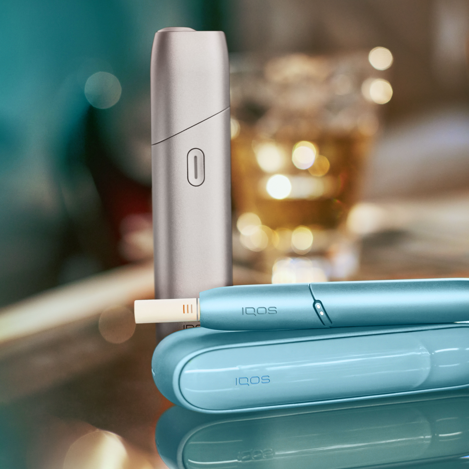IQOS ORIGINALS ONE in Silver und IQOS ORIGINALS DUO in Turquoise auf einem Tisch