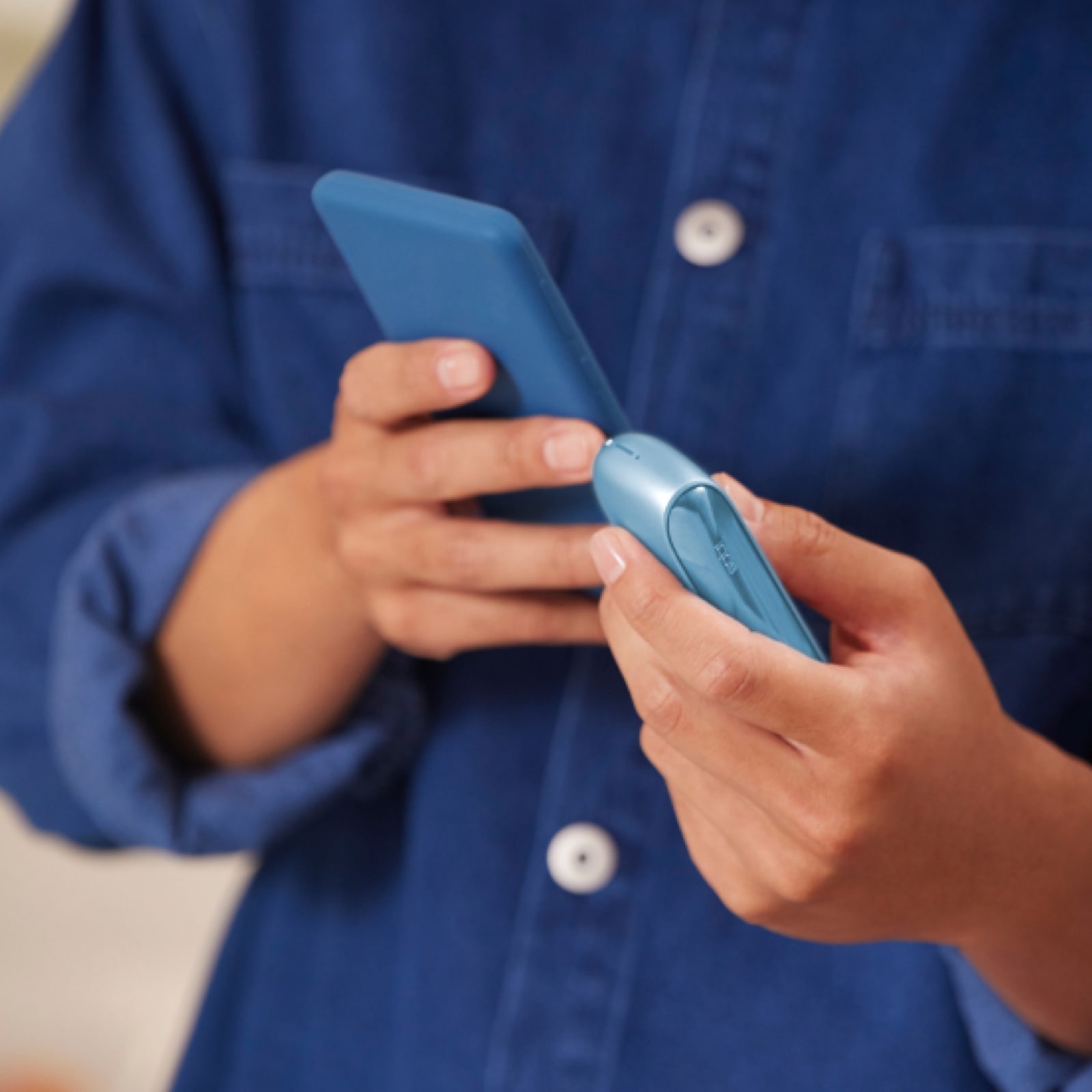 Ein Mann im blauen Hemd hält ein Smartphone und ein IQOS-Gerät in den Händen