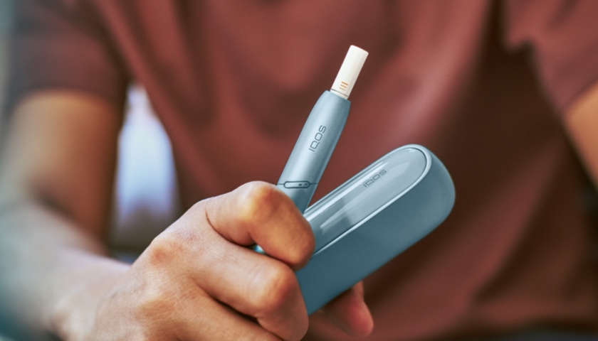 Man holding IQOS ORIGINALS DUO charger and holder with an inserted HEETS stick