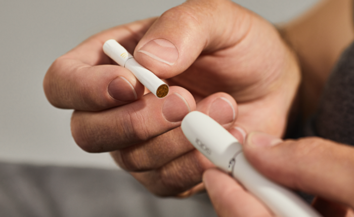 Hand inserting tobacco stick in white IQOS DUO Holder