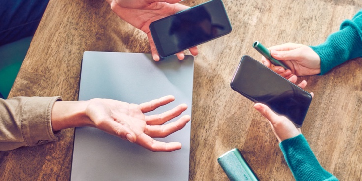 Hands holding smartphones and one IQOS device. Hands holding smartphones and one IQOS device.