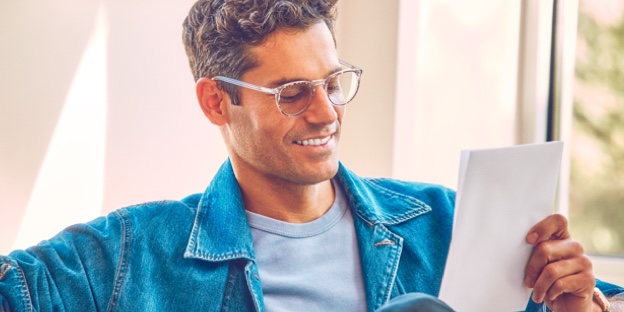 A man wearing glasses reading a warranty brochure.